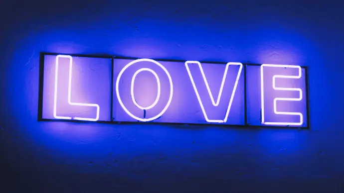 Neon sign reading “LOVE” in blue light, representing themes of care and restoration.