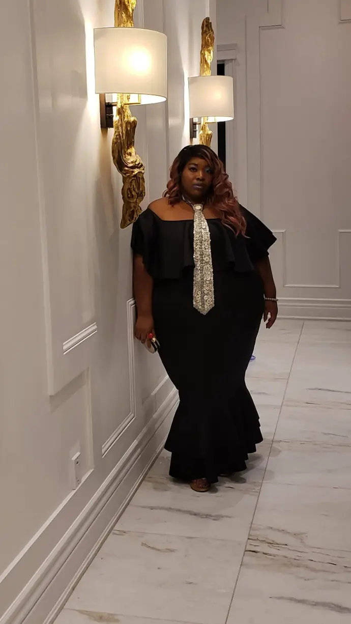 Cola, founder of Lips and Language, standing in a hallway wearing a black dress, representing presence and grounded leadership.