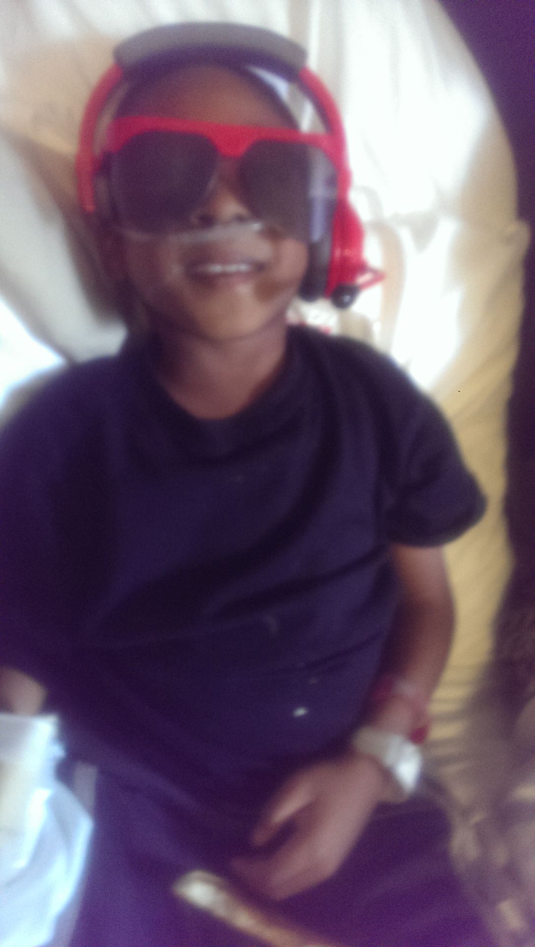 Child standing indoors wearing a dark shirt, smiling at the camera.
