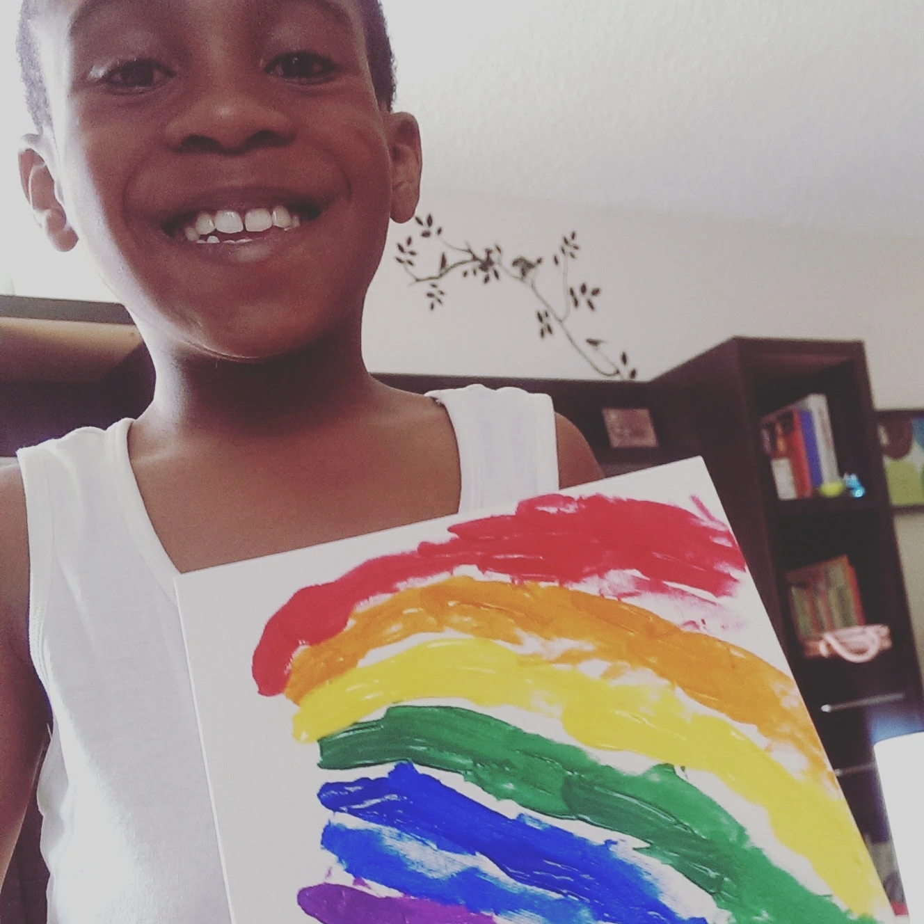 Smiling child holding a rainbow-colored drawing.