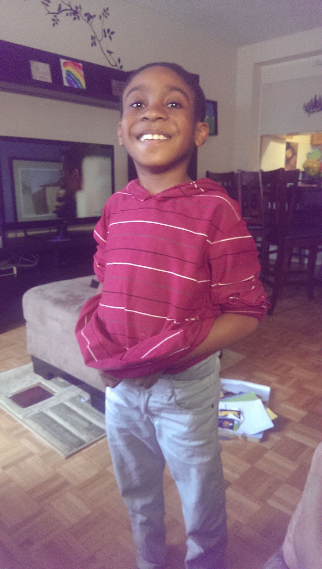 Child wearing a red sweater standing in a room with books.