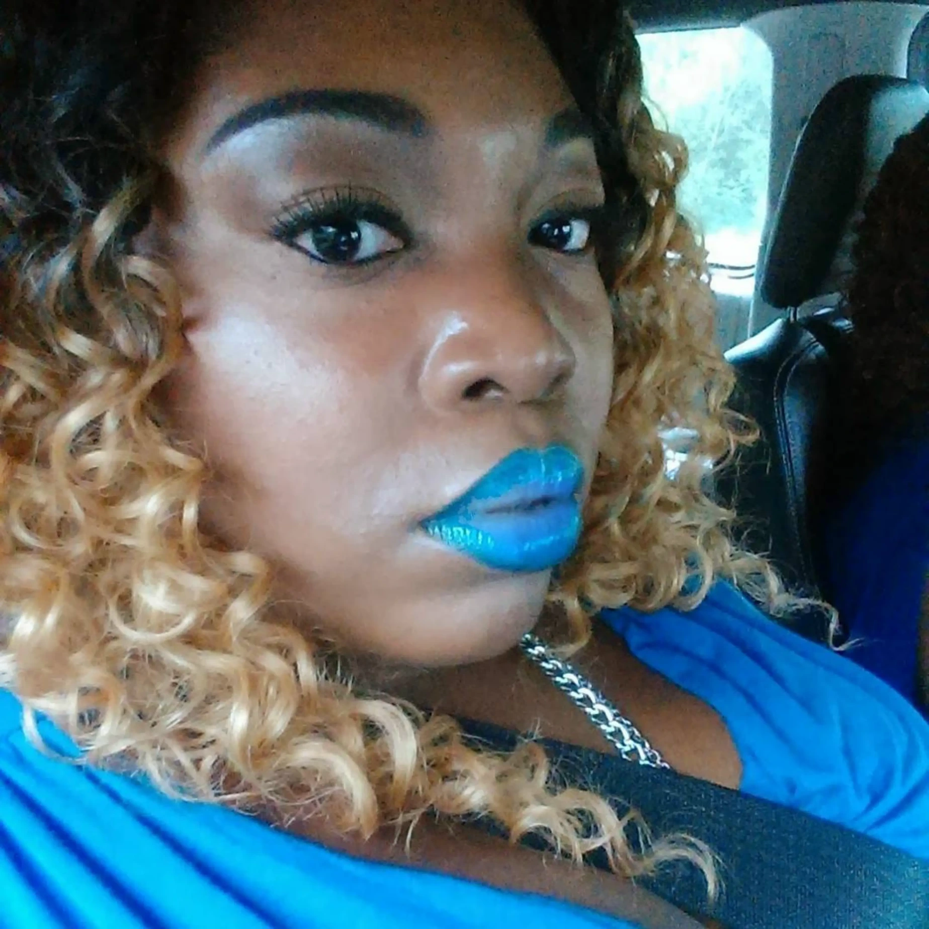 Close-up portrait of a woman with blue lipstick and curly blonde hair.
