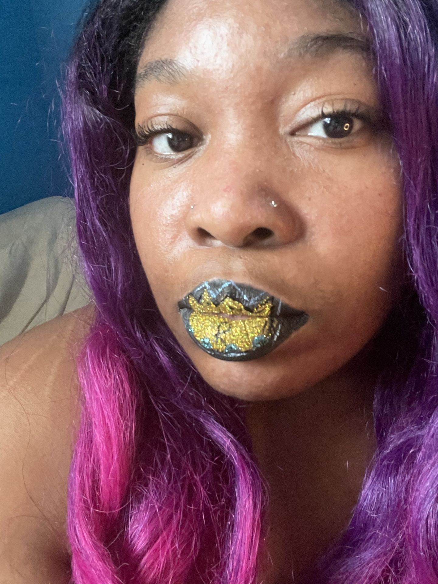 Black woman with blue glitter lips and silver eyeshadow, close-up portrait featuring shimmering editorial makeup and purple ombré hair