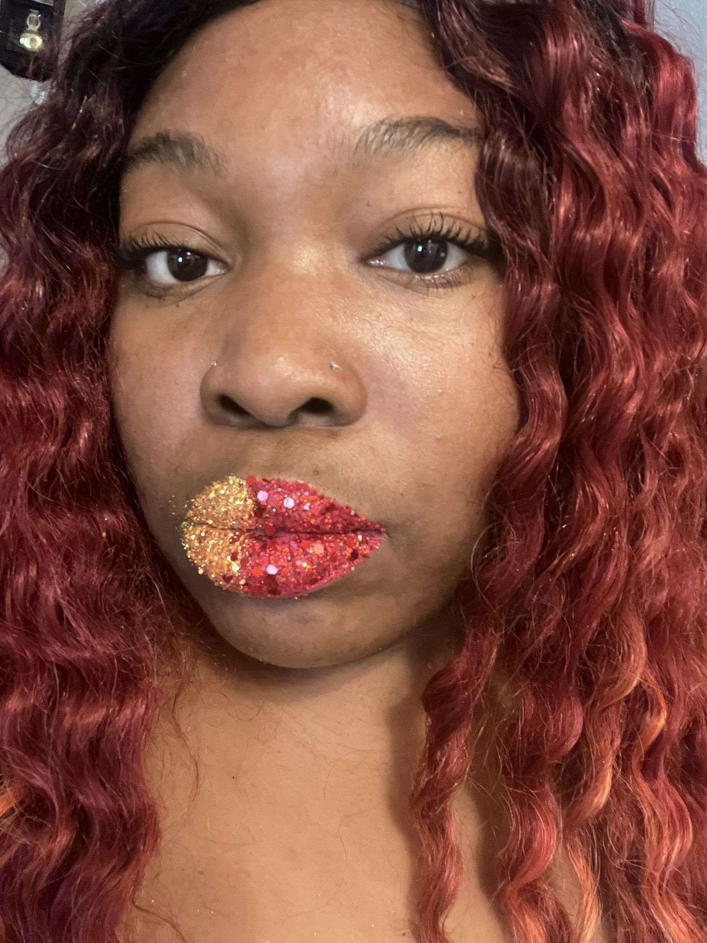 Black woman with deep red curls and glossy red lipstick, close-up beauty image emphasizing warm tones and luminous skin