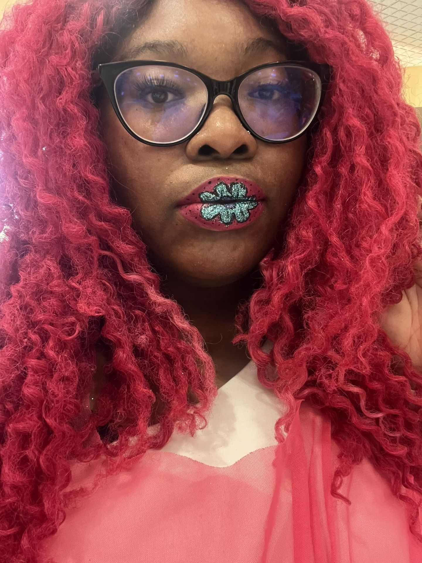 Black woman with red curls and gold-flecked lip design, close-up portrait highlighting jewel-tone shimmer and artistic makeup styling