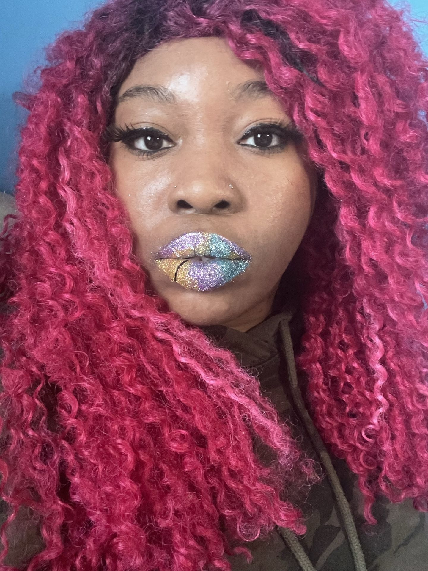 “Close-up of woman with bright pink braids wearing multicolored glitter lip art.”