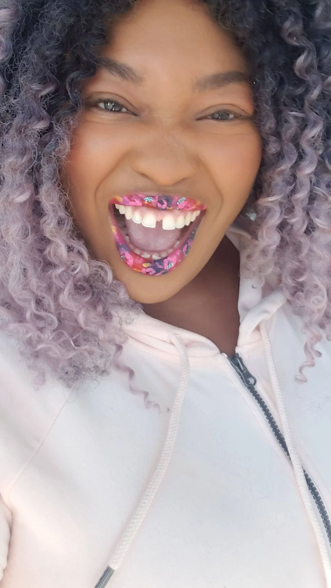 Woman smiling with lilac curls and multicolor glitter lip art