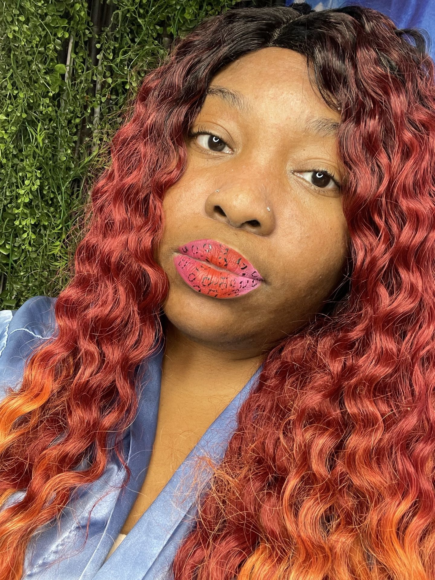 Woman with red curls in a blue top wearing soft coral lipstick