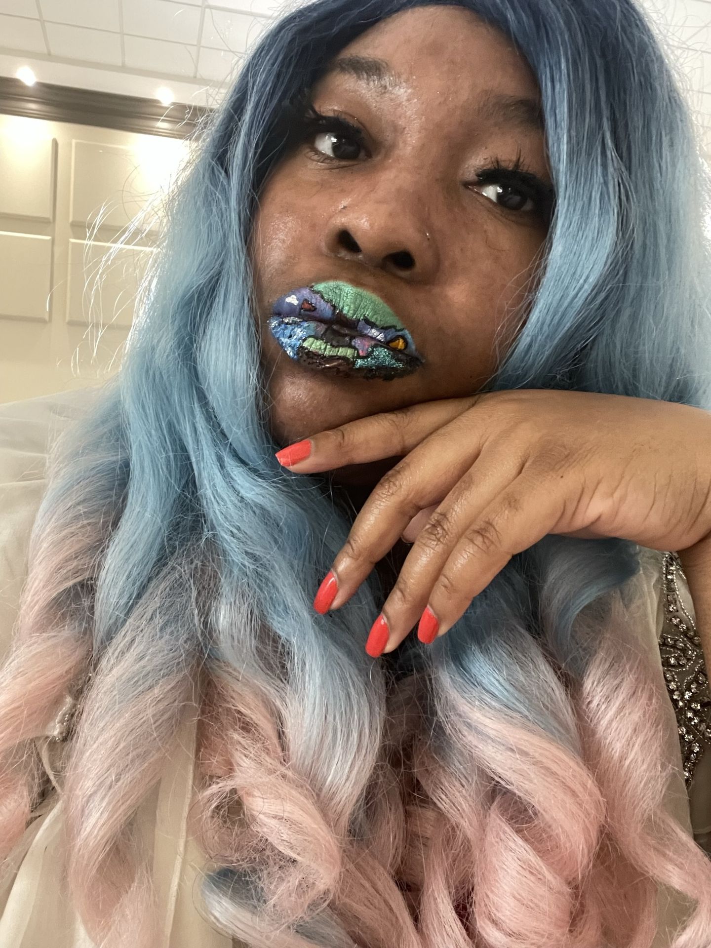 Woman with silver-blue hair and gold crystal lip accents, resting her hand near her face