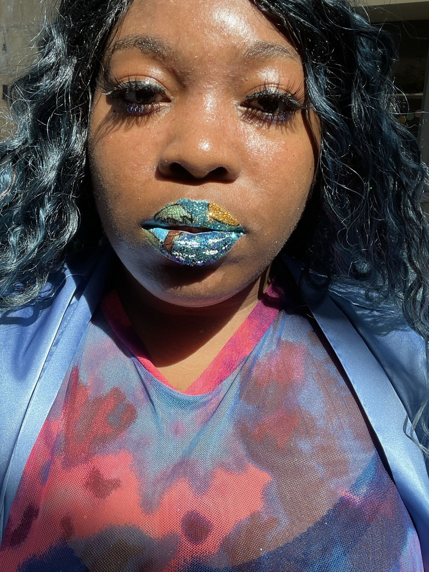 Woman with dark hair and aqua rhinestone lip pattern against a denim jacket